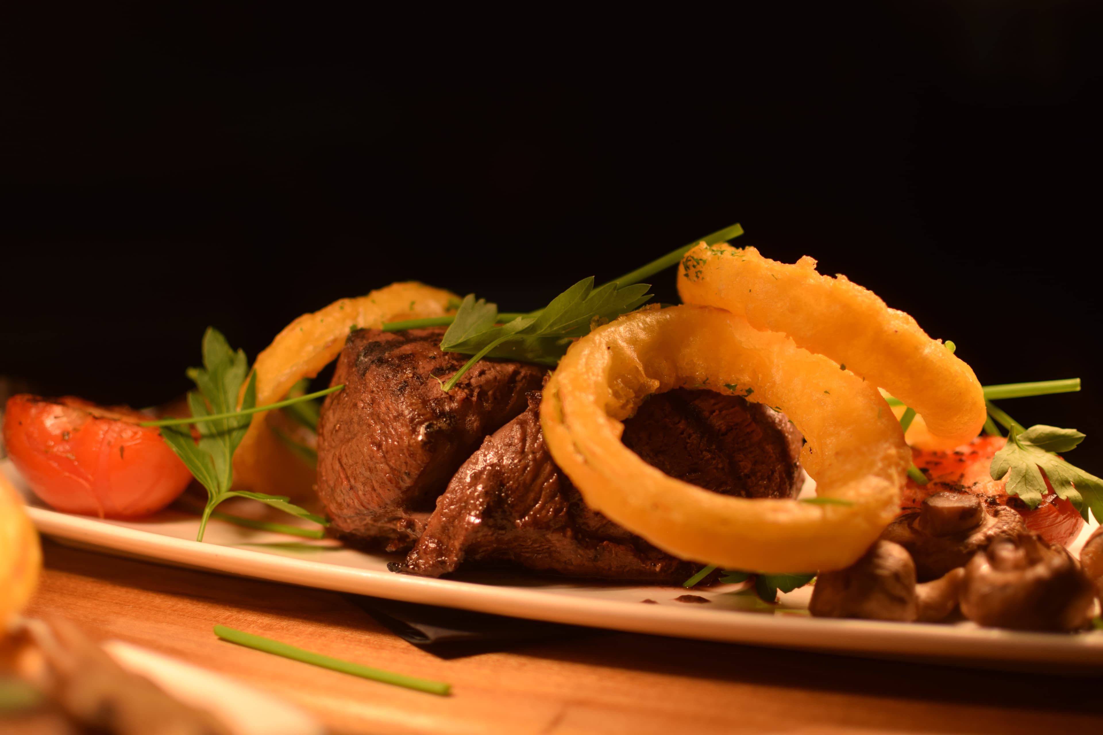 Steak on a plate with onion rings, mushrooms, and tomato